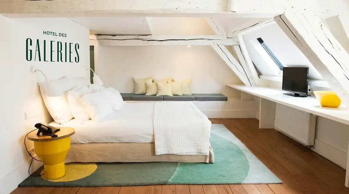 Suite luminosa de Hôtel des Galeries bajo bóvedas blancas, con el logotipo oficial integrado con elegancia