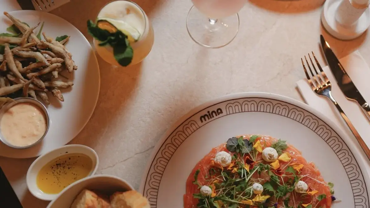 A table set at Mina in Ixelles: carpaccio, fried starters, bread and a cocktail on pale marble.