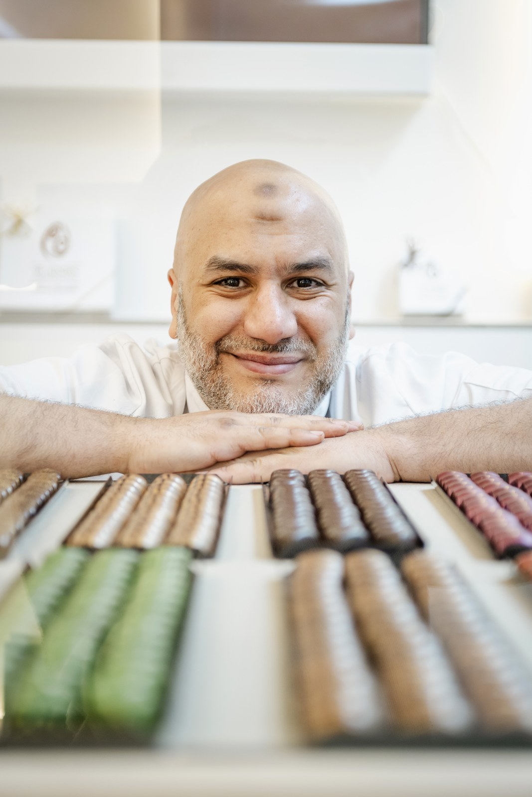 Retrato de Youcef Amar detrás de una selección de chocolates de Plaisirs Chocolatés, fotografía del sitio oficial