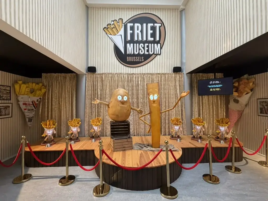 Friet Museum Brussels: Kartoffel- und Pommes-Maskottchen unter dem Museumsschild — © Friet Museum Brussels